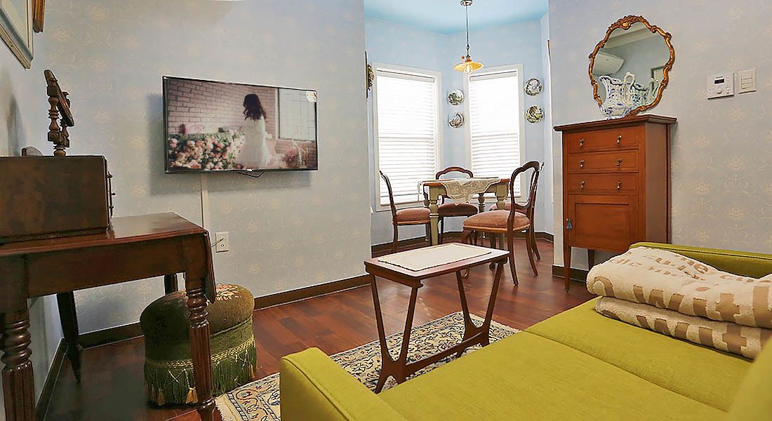 A living room with a television, a dining table with chairs, a sofa, and a wooden cabinet.