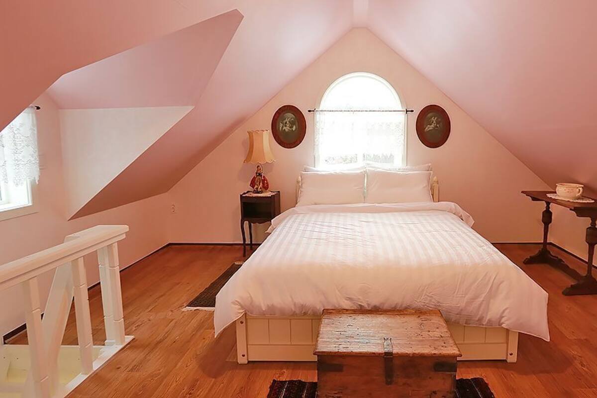 A bedroom with a sloped ceiling, a bed, a nightstand, a small table, and a window.