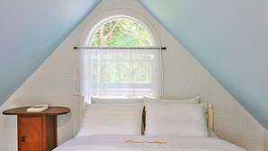 A triangular room with a bed, a small table, and a window with a curtain. - Kismet Cottage (Pyeongchang)