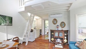 A spacious living area with a wooden floor, a dining table with chairs, a blue sofa, a wooden cabinet with decorative items, and a staircase leading to an upper level. - Kismet Cottage (Pyeongchang)