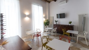 A modern dining area with white tables and chairs, a wooden cabinet, and a television on the wall. - Savoy Riviera (Naples)