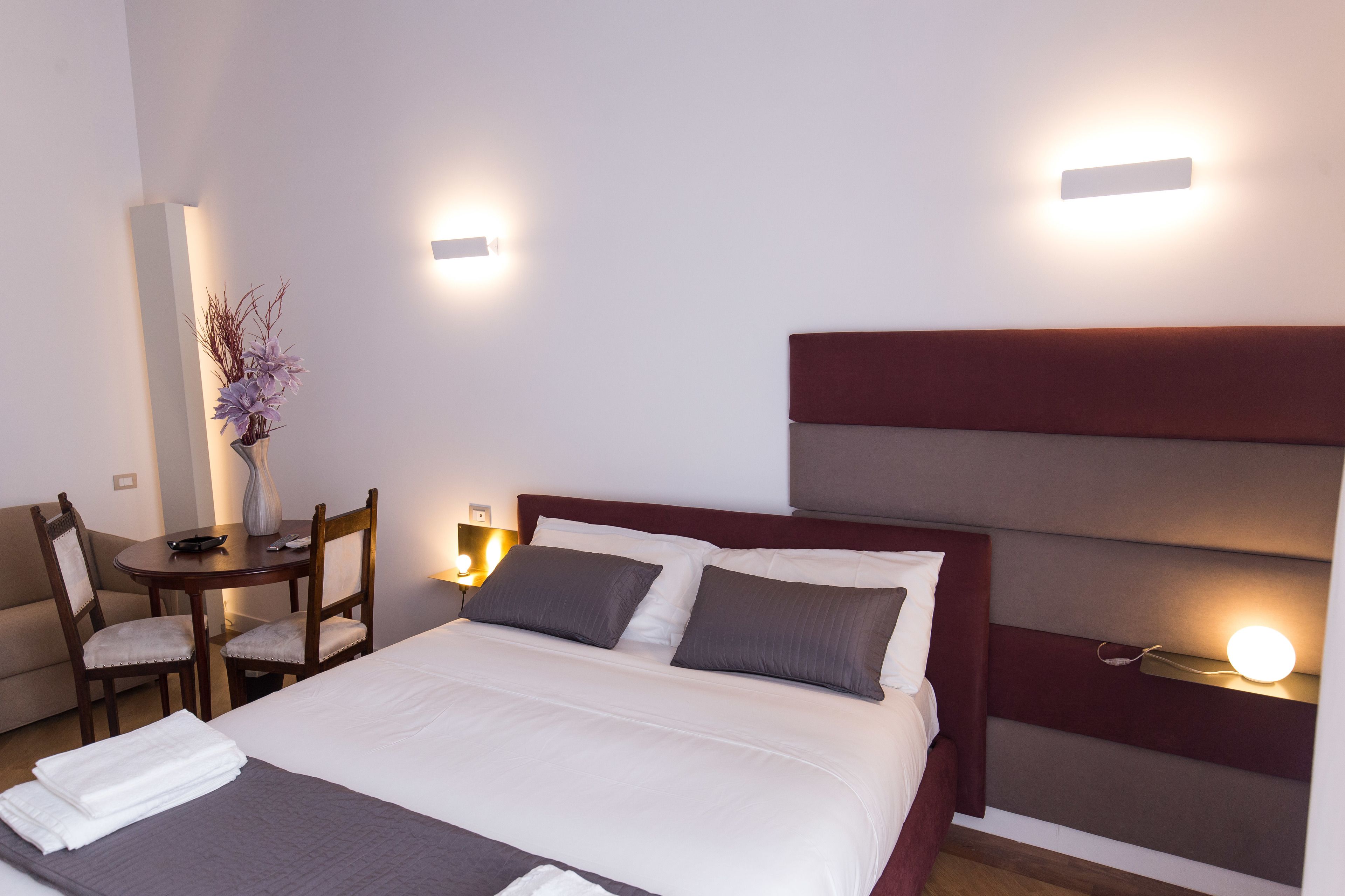 Une chambre d’hôtel comprenant un lit, des tables de chevet, un bureau, des chaises et des lampes fixées au mur.