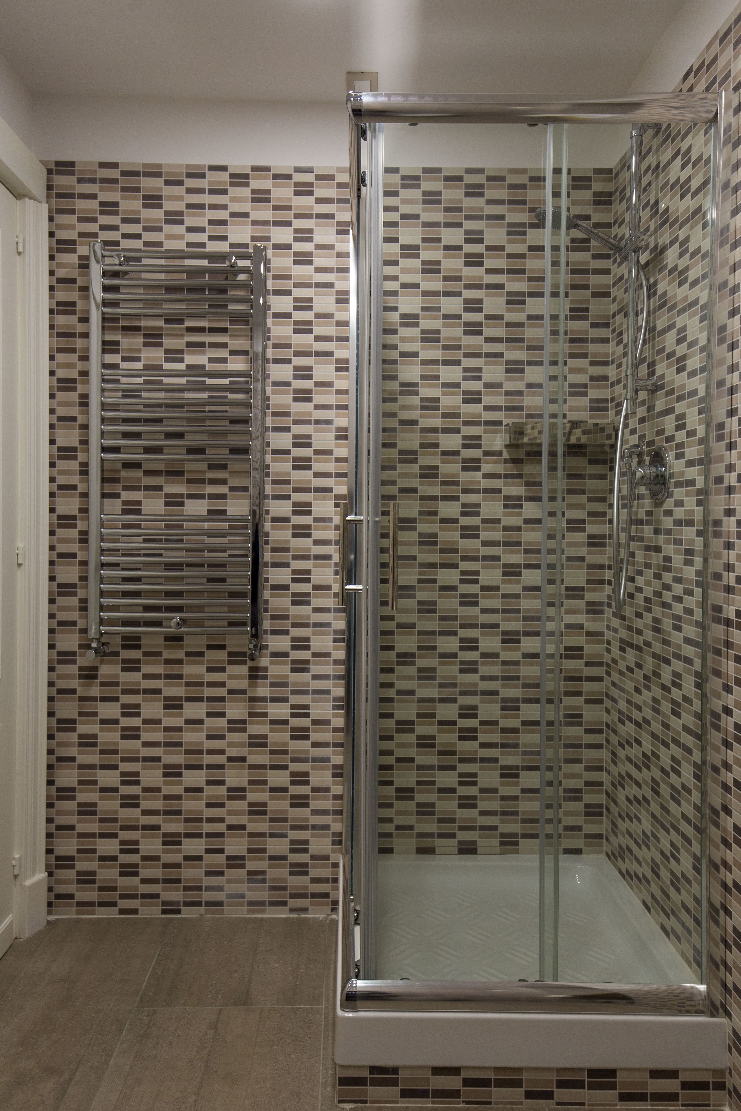 Une salle de bain moderne dotée d’une douche à parois de verre, d’un porte-serviettes intégré et d’un pare-feu en carreaux.