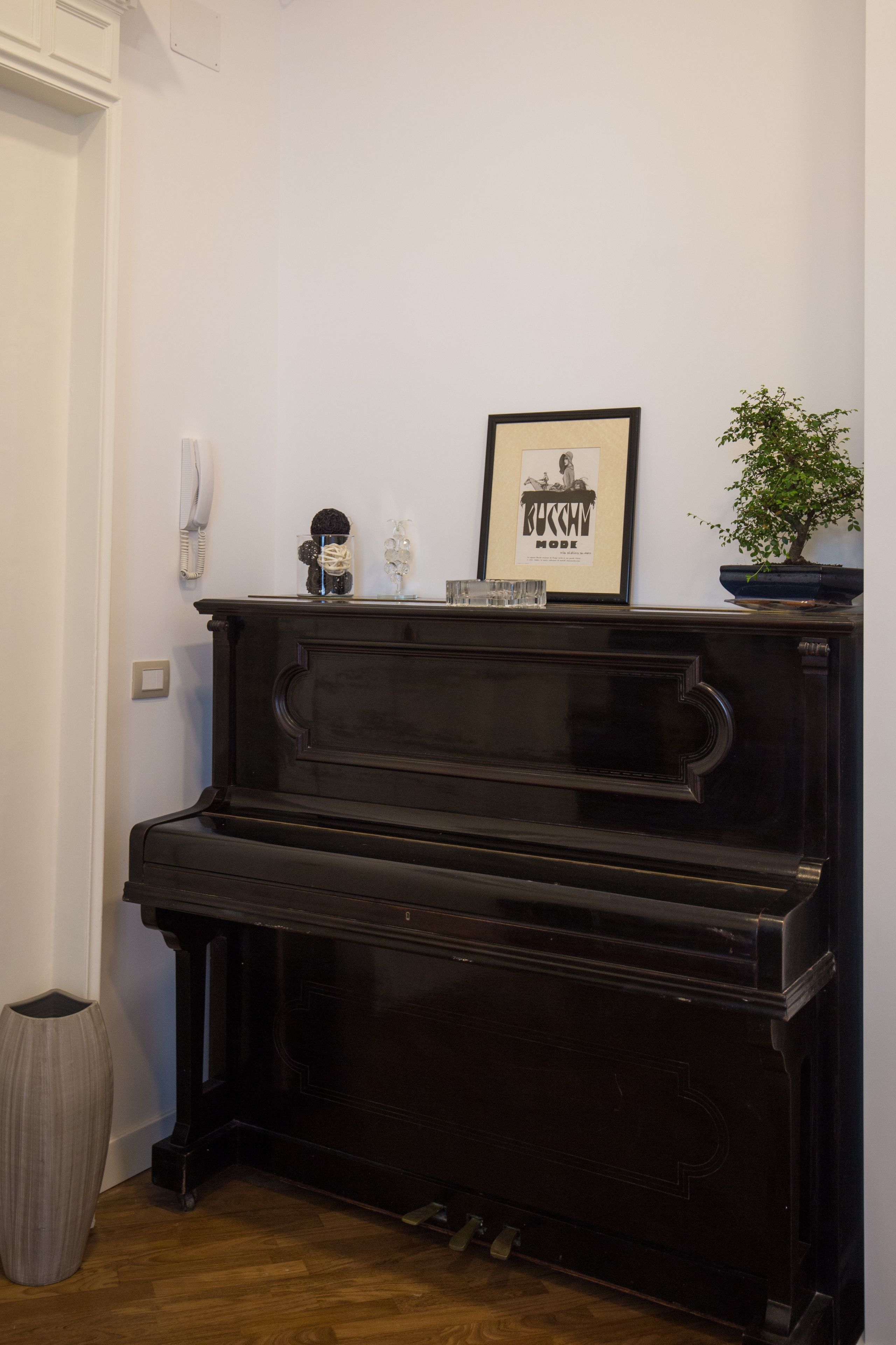 Un piano noir orné de quelques objets décoratifs, un tableau encadré et une plante en pot.