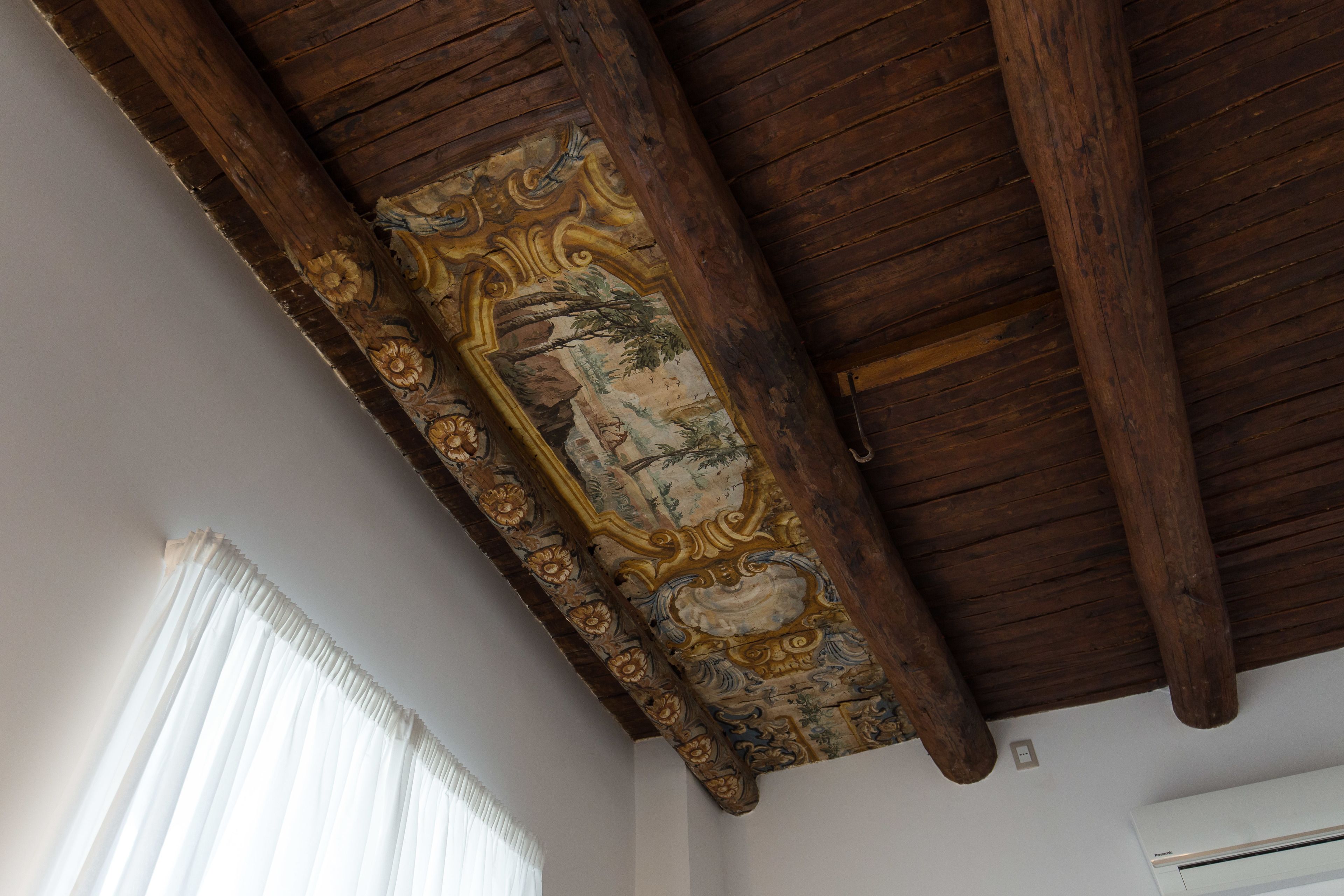 A room with a wooden ceiling, a decorative panel with floral and foliage designs, and a white air conditioning unit.