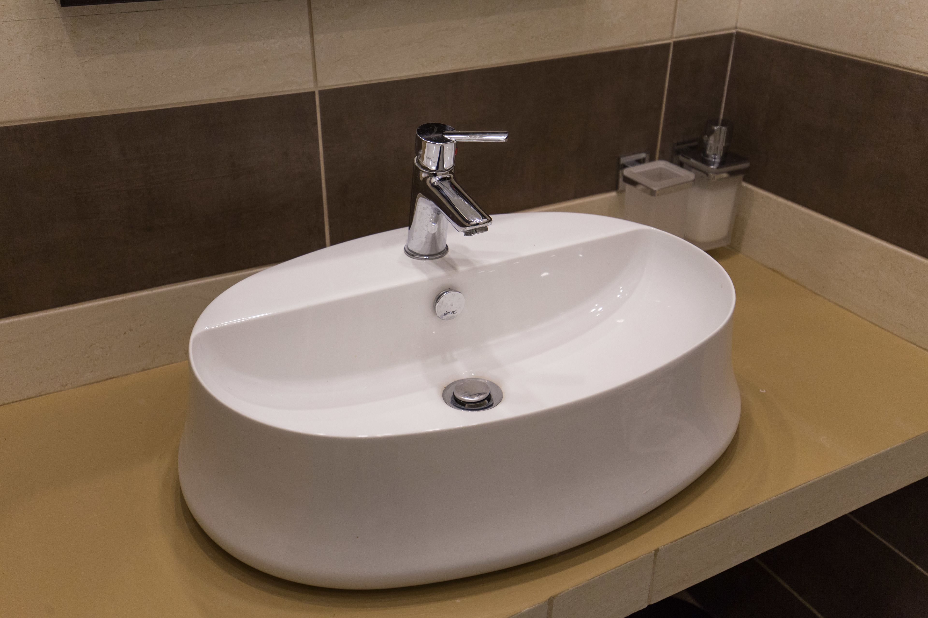 A white bathroom sink with a chrome faucet, a small trash bin, and a beige countertop.