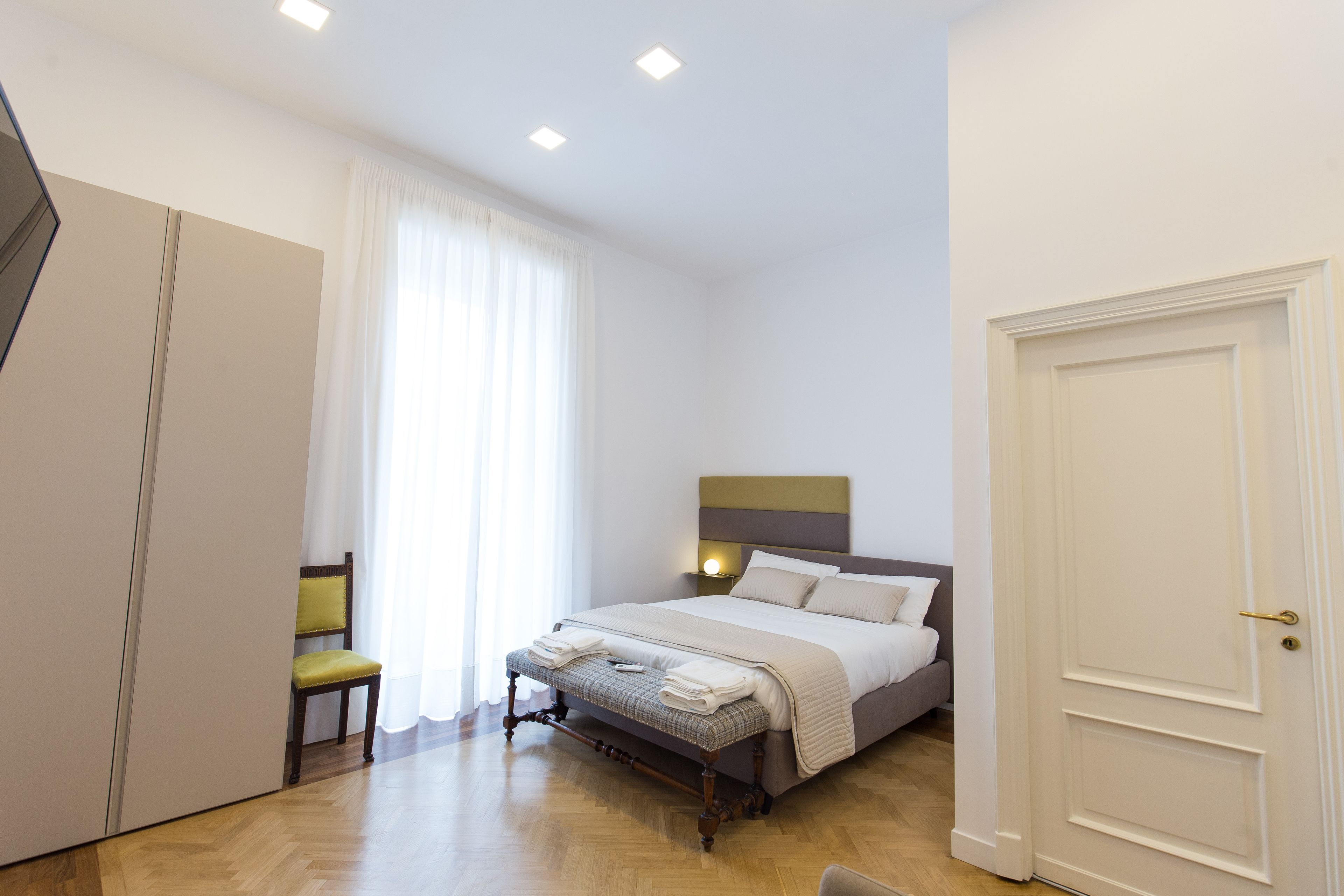 A bedroom with a bed, a chair, a wardrobe, and a door.