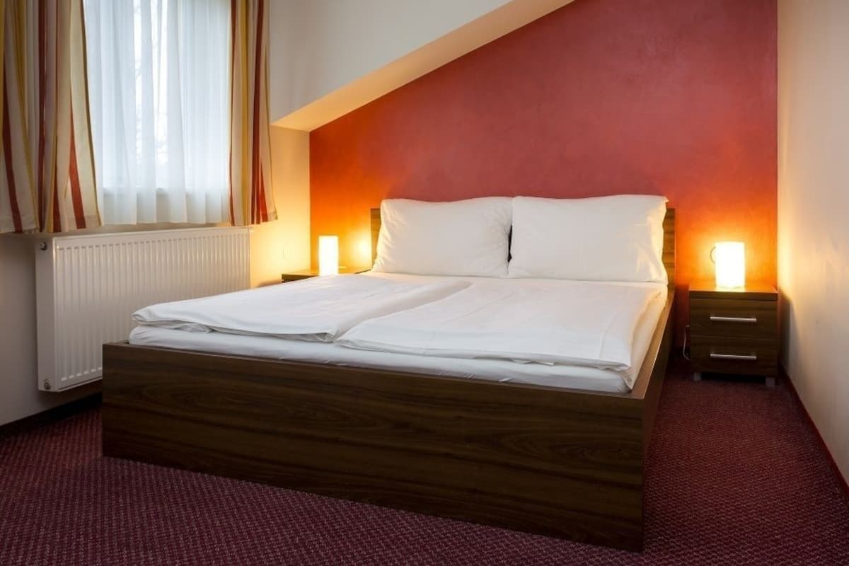 A bedroom with a wooden bed, two bedside tables, a window with curtains, and a red accent wall.