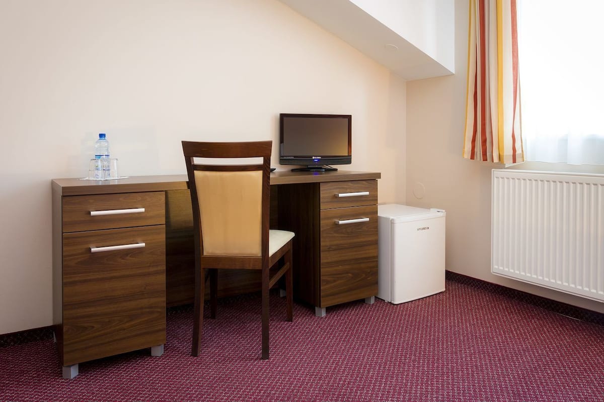 A hotel room with a wooden desk, a chair, a small white fridge, and a radiator.