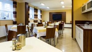 A hotel dining area with multiple tables, chairs, a TV mounted on the wall, and a kitchen counter with glasses. - Pension Bed & Breakfast (Kutna Hora)