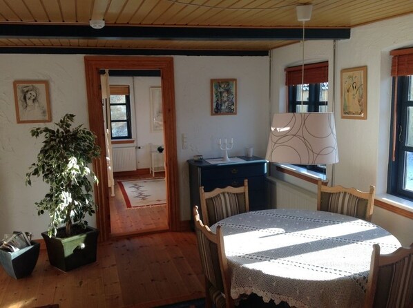 A cozy room with a wooden ceiling, a round table with a lace tablecloth, a potted plant, and a blue cabinet. - Stevns Klint Bed & Breakfast (Store Heddinge)