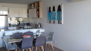 Ein modernes Wohnzimmer mit einem Glastisch, grauen Sofas und einer Küche im Hintergrund.