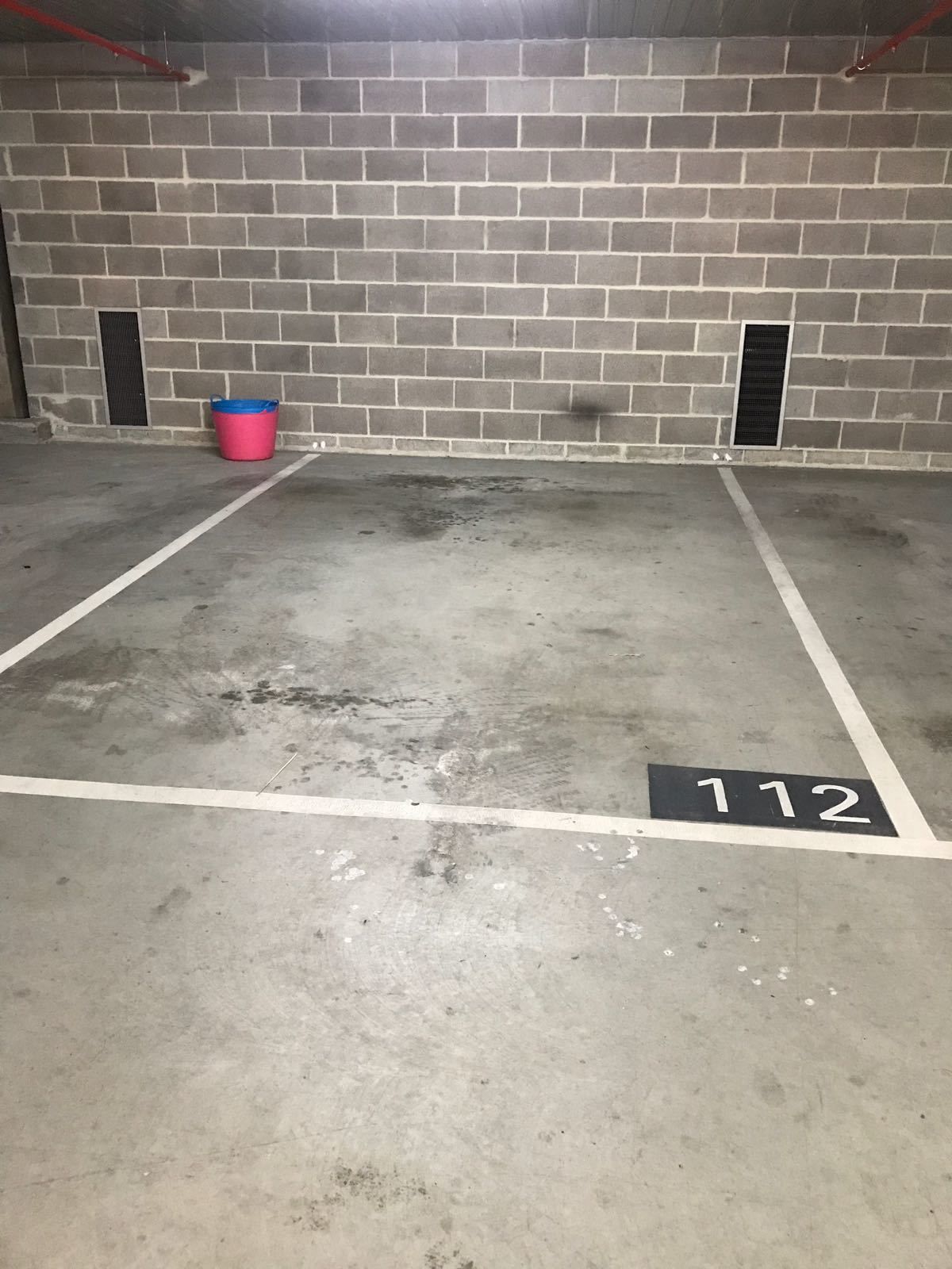 Eine Tiefgarage mit Betonböden, gekennzeichneten Parkplätzen und einer Ziegelwand.