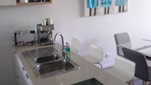 Eine moderne Küche mit Spüle aus Edelstahl, Kaffeemaschine und Mikrowelle. Es gibt einen Essbereich mit Tisch und Stühlen.
