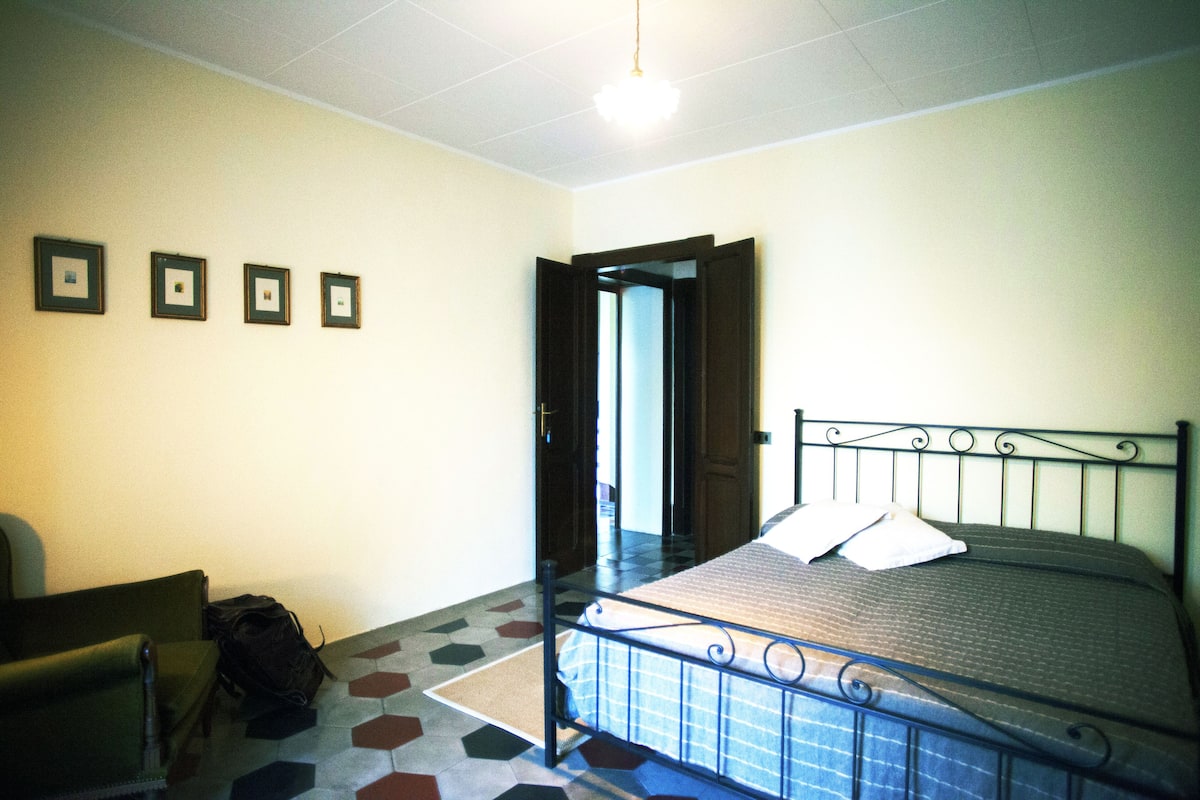 Una habitación con una cama, una silla y una puerta que da a otra estancia.