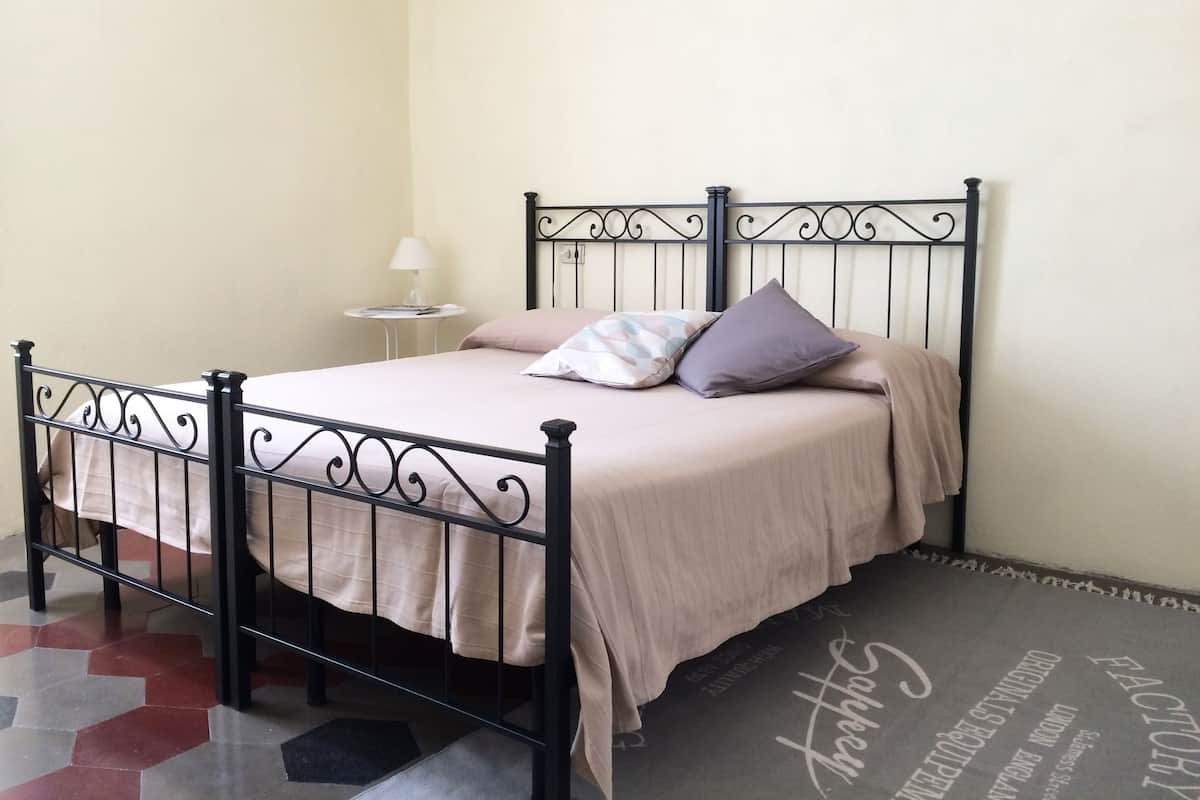 Una cama con estructura metálica, una colcha color beige y dos almohadas.