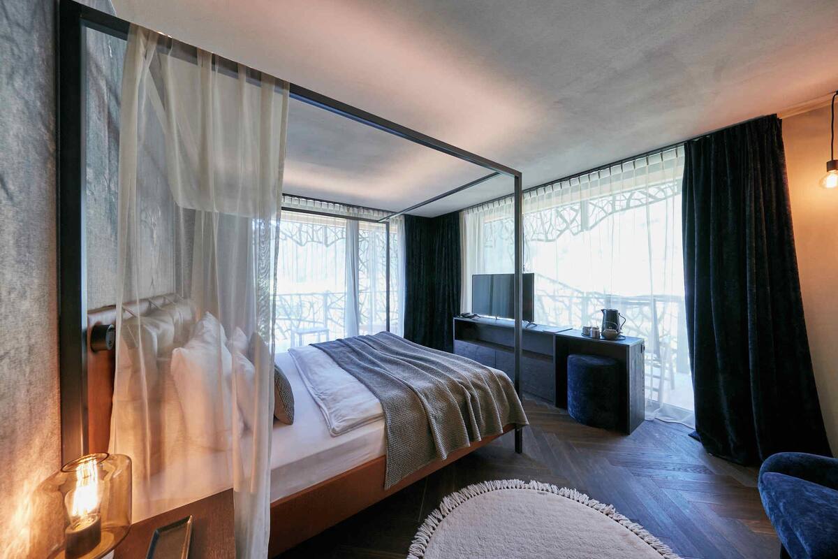 A modern bedroom with a large bed, a bedside table, a TV, and a view of a bridge.