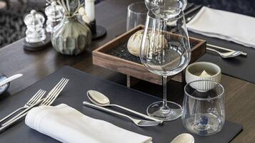 Una mesa de comedor con un mantel individual negro, un mantelino blanco doblado, cubiertos y copas de vino transparentes.