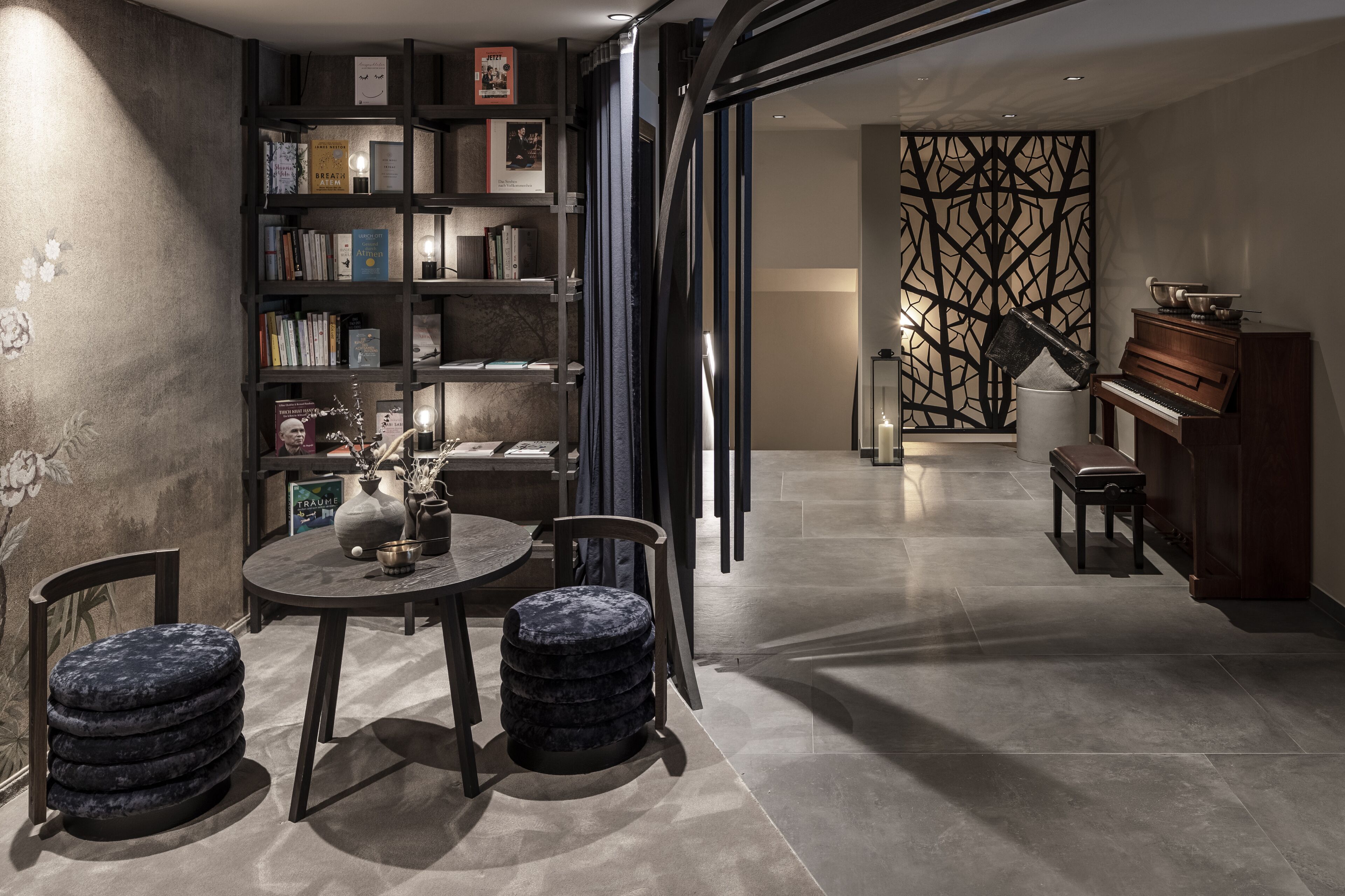 Una sala de estar moderna con una estantería de madera oscura, una mesa redonda con dos sillas, un piano y un panel decorativo en la pared.