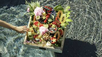 Une caisse en bois remplie de fruits, de légumes et de fleurs, suspendue au-dessus d’une étendue d’eau.
