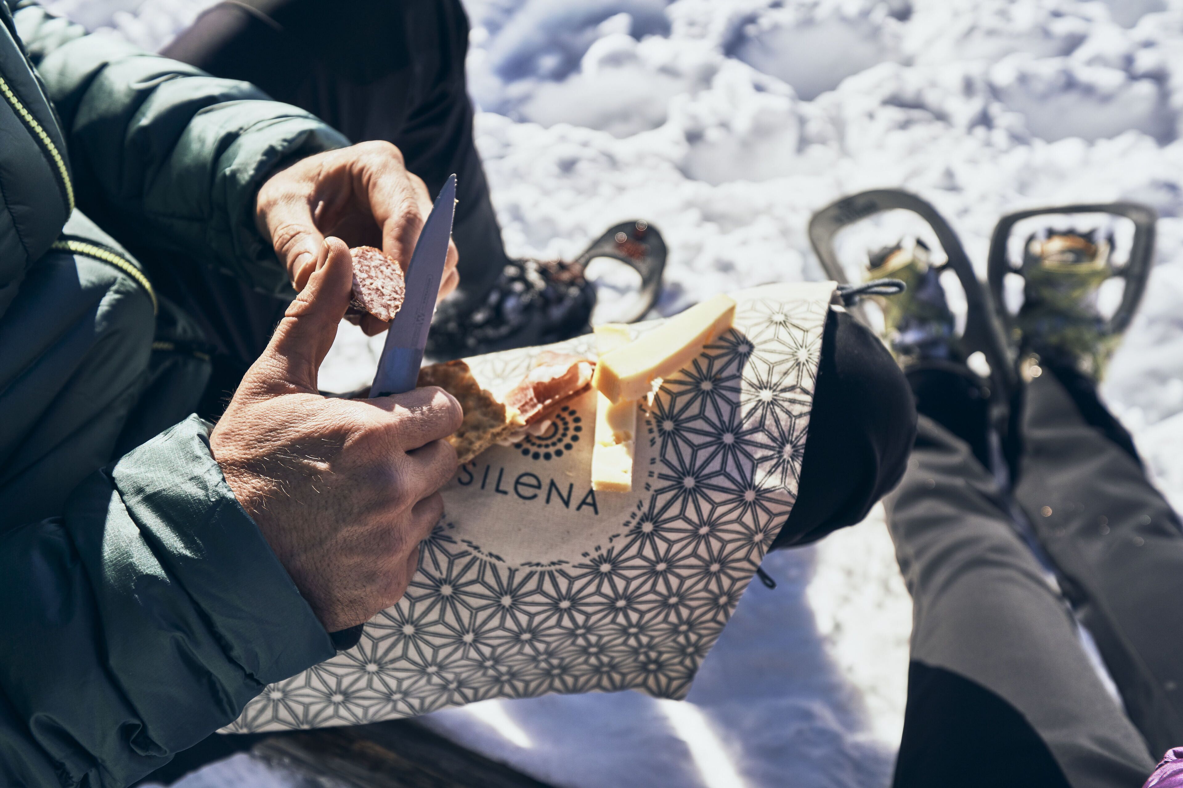 A person holding a sandwich wrapped in a patterned paper bag labeled "SILENA."