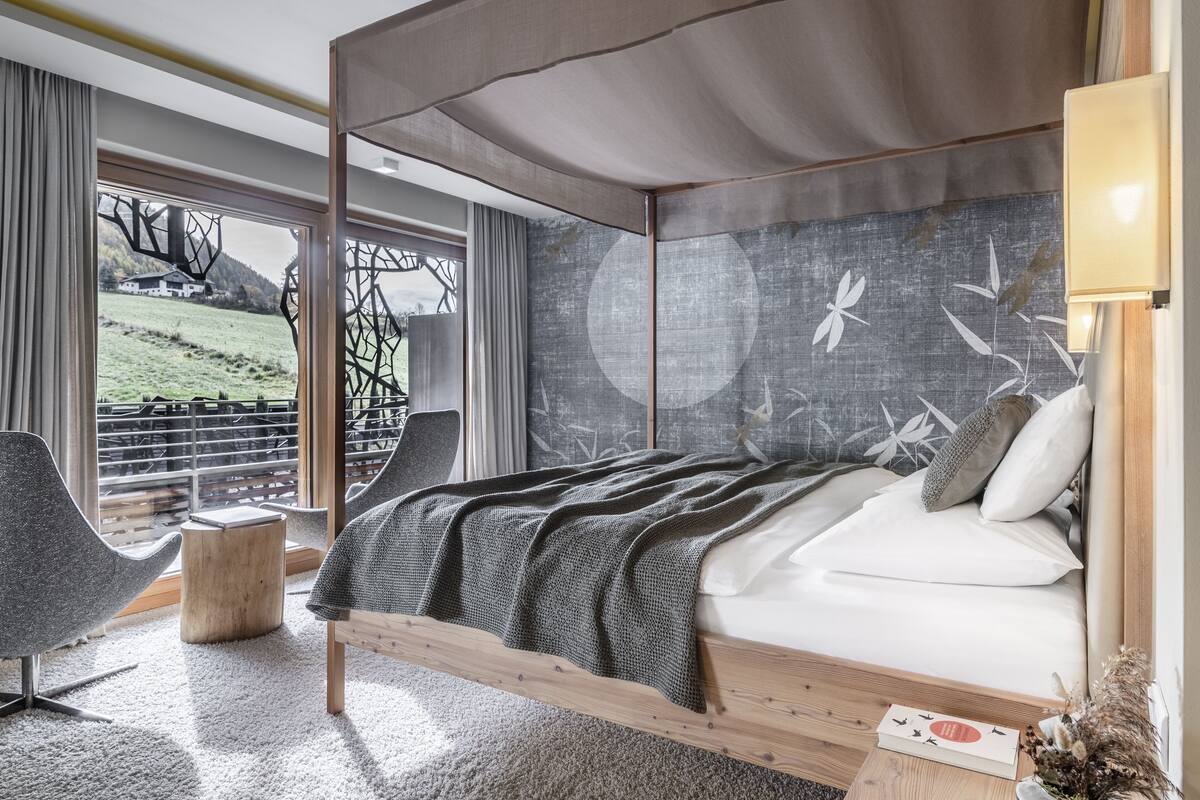 A modern bedroom with a large bed, a view of a green landscape, and a unique wall art piece.