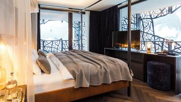 A modern bedroom with a large bed, a desk with a TV, and a view of a snowy landscape.