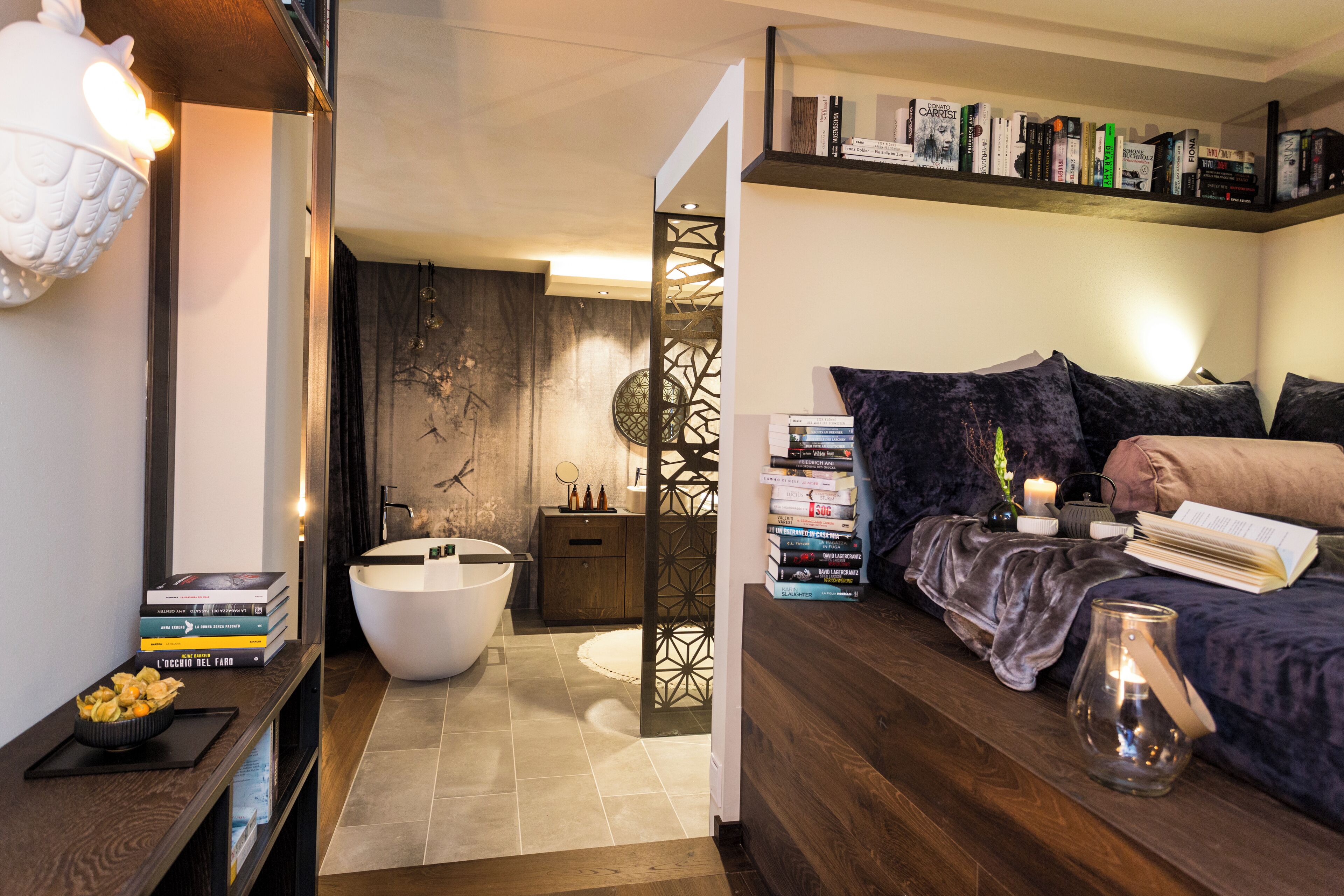 A modern bedroom with a large bed, bedside books, a white bathtub, and a wooden floor.