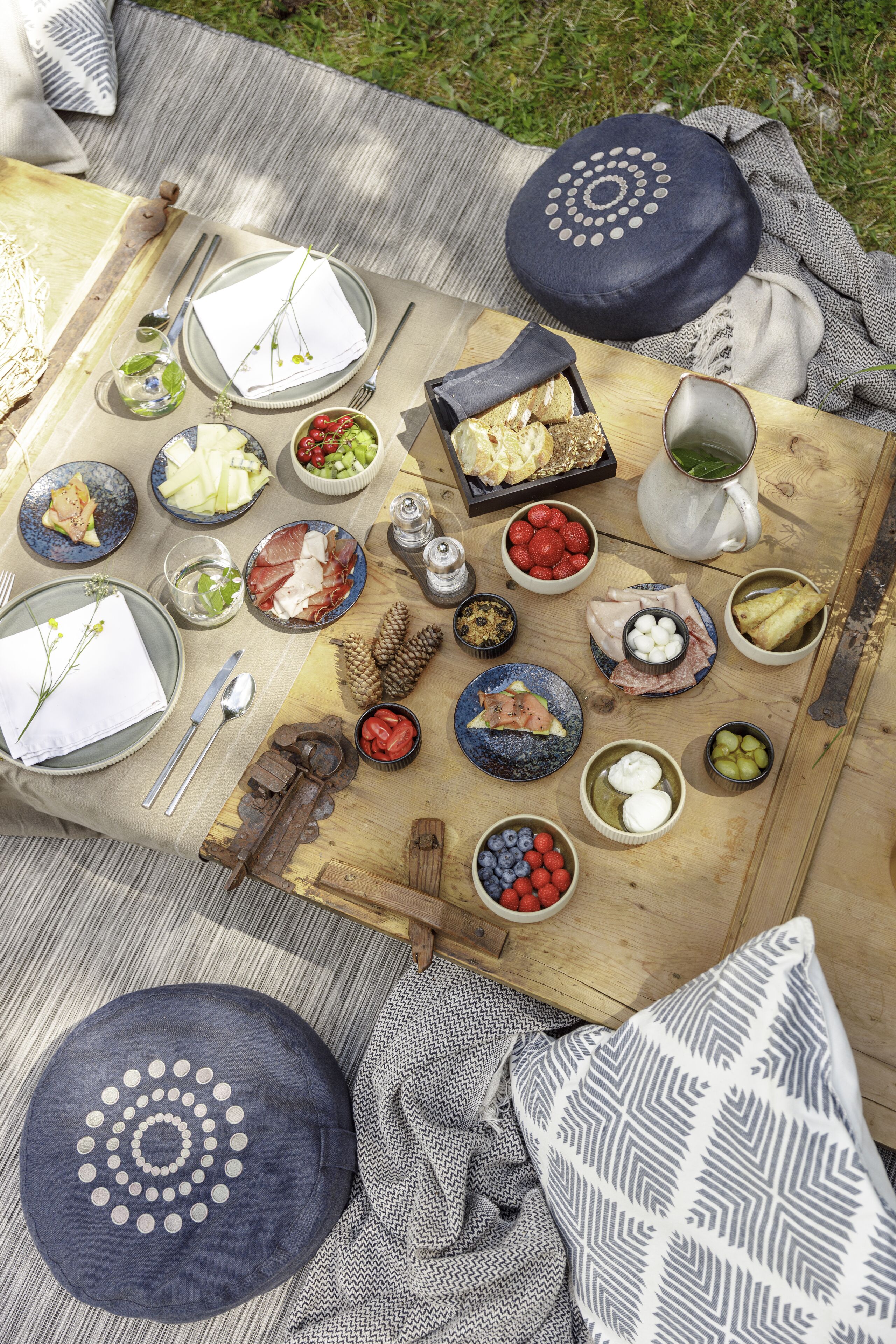 Un montaje para picnic con diversos alimentos y utensilios sobre una manta.