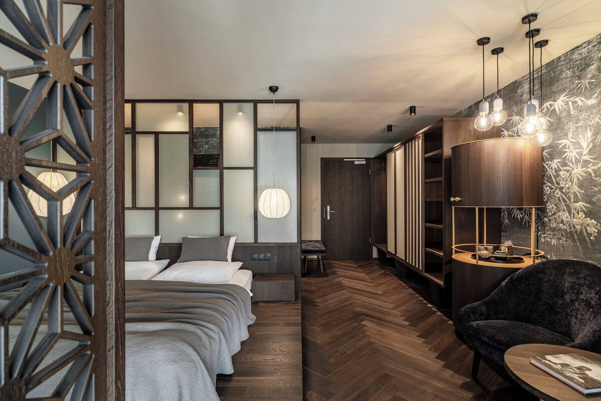 A modern hotel room with a large bed, a seating area with a chair and table, and a wardrobe with a mirror.