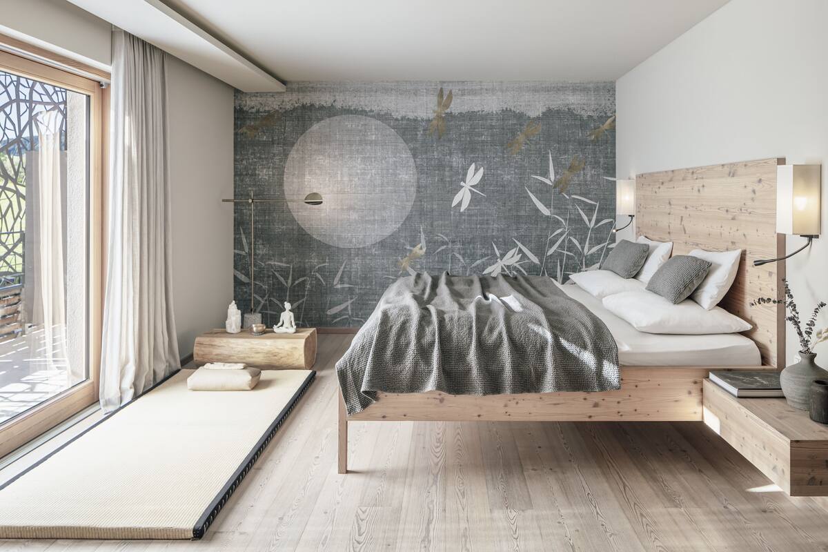 A modern bedroom with a minimalist design, featuring a bed with a wooden frame, a large wall mural, and a view of the outdoors through a window.