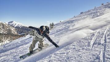 A person snowboarding down a snowy slope with a clear sky and mountains in the background.