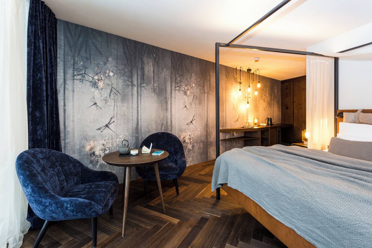A modern hotel room with a large bed, two chairs, a small table, and a wall with a nature-themed mural.