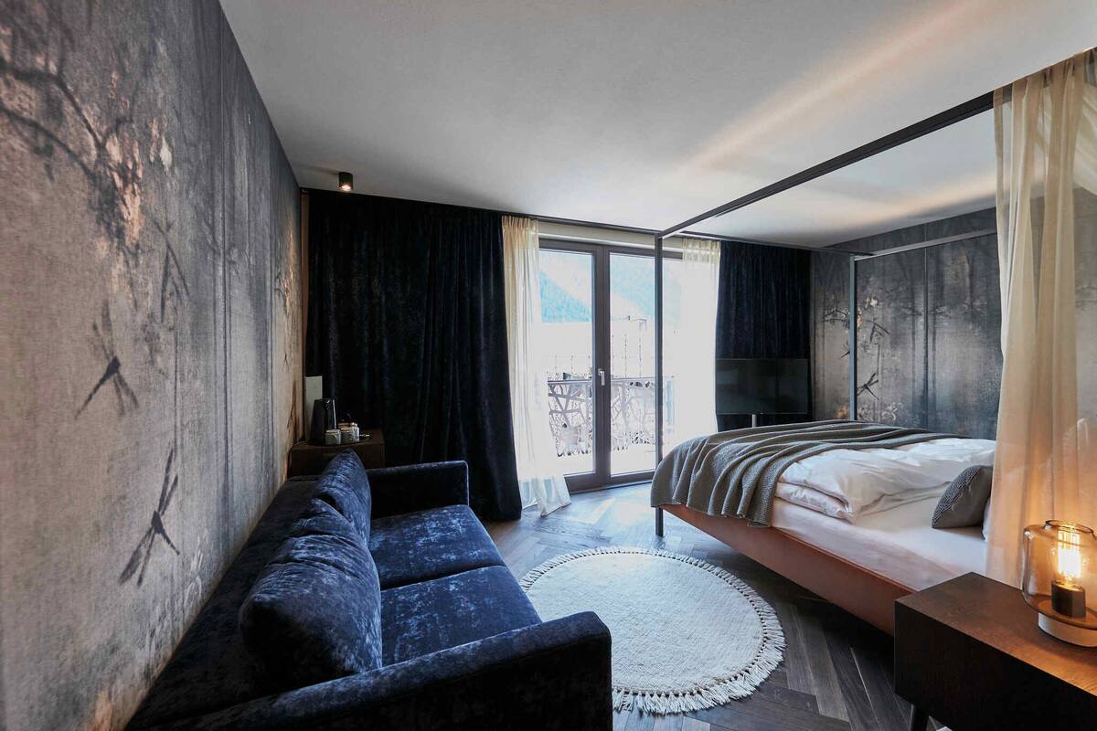 A modern bedroom with a large bed, a sofa, a round rug, and a view of the outdoors through a sliding door.