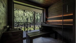 Una cuina moderna amb una banca de fusta, un fogó encastrat i vista a un bosc a través d'una finestra amb un panell decoratiu.