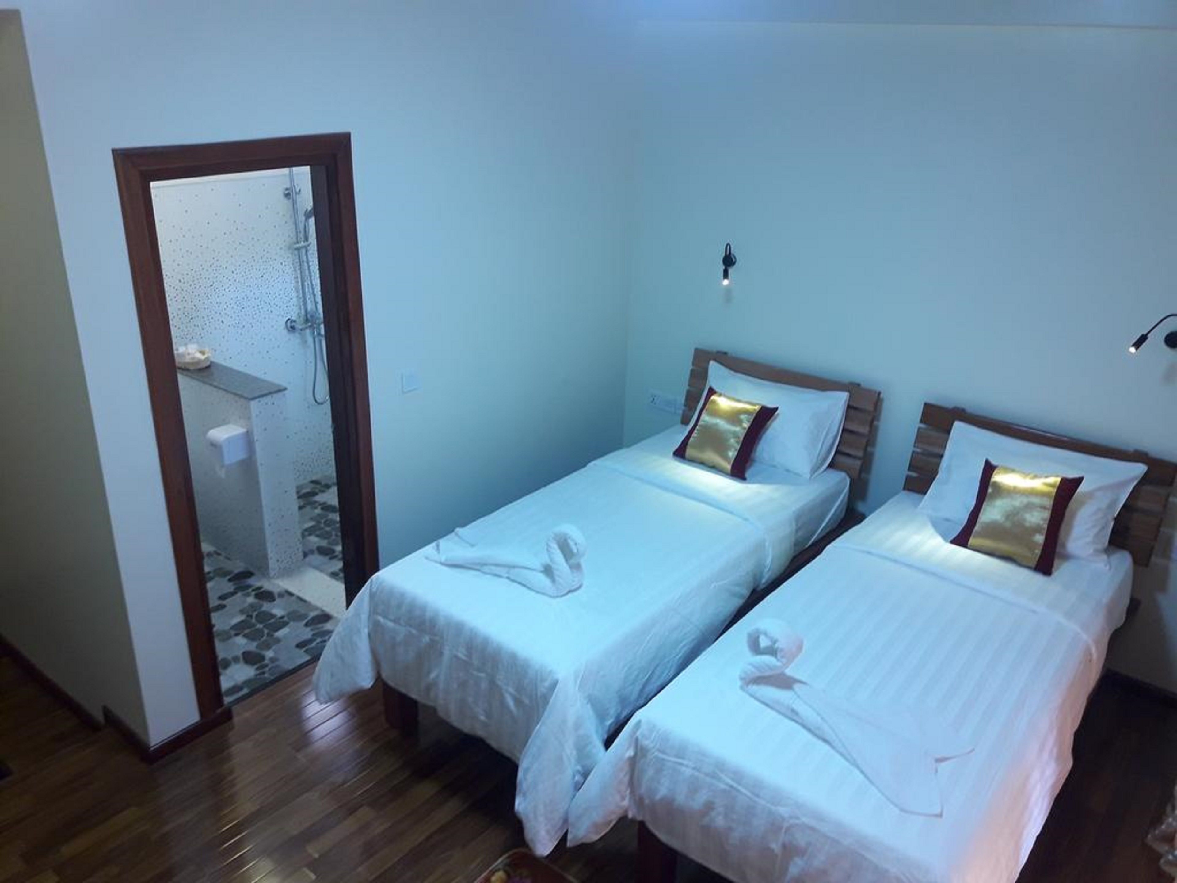 Habitació d'hotel amb dos llits individuals, sòl de fusta, bany petit amb plat de dutxa i mirall.