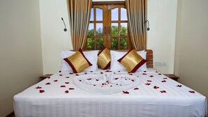 A neatly made bed with white linens, gold and red pillows, and a heart-shaped arrangement of rose petals. - Ocean Ngapali Lodge (Ngapali)