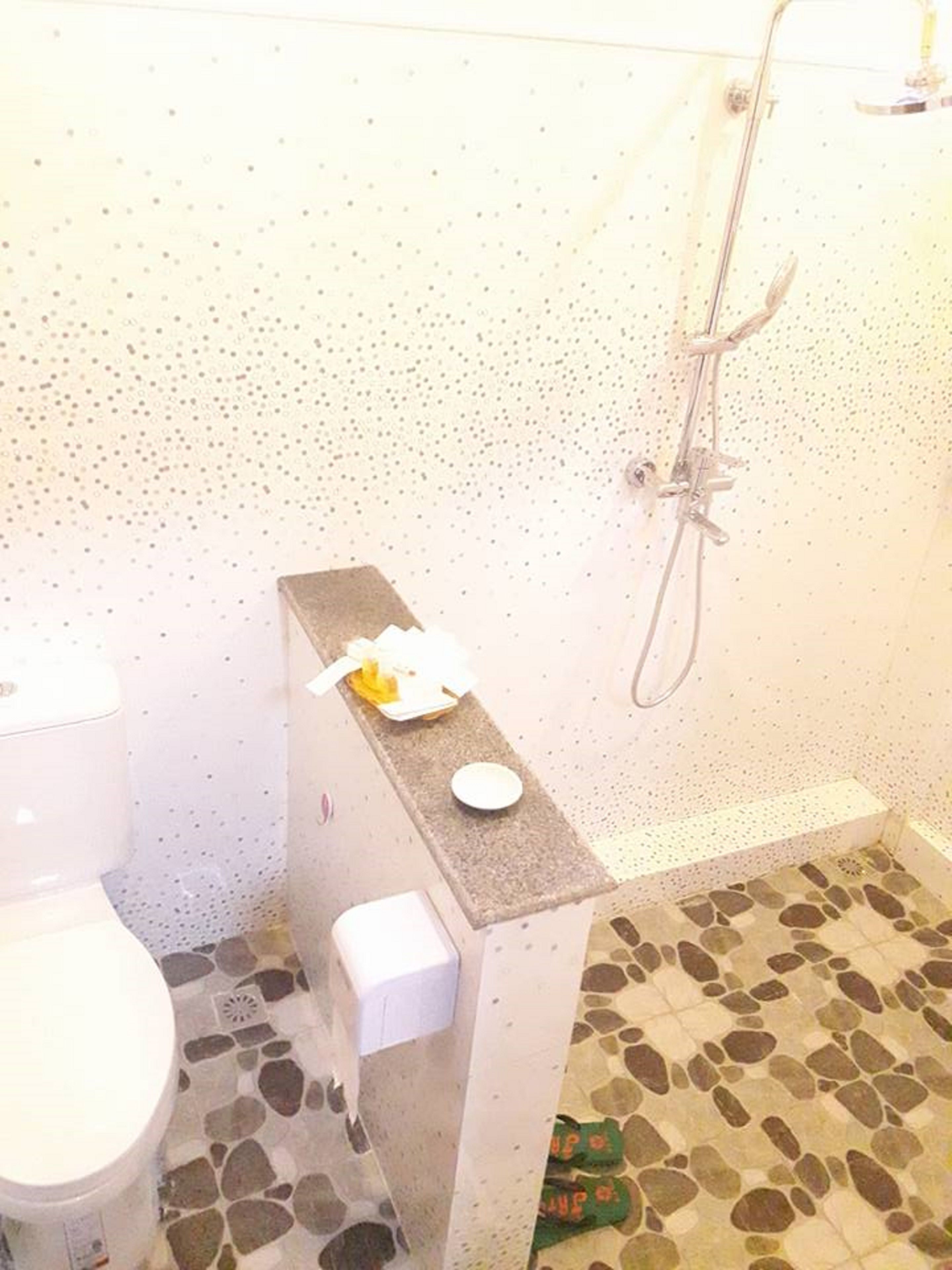 Un baño con inodoro, ducha y lavamanos con jabonera.