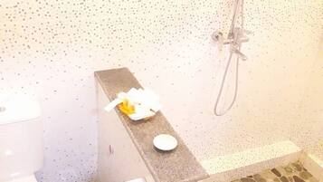 Un baño con inodoro, ducha y lavamanos con jabonera.