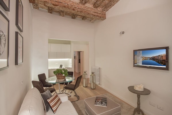 A modern living room with a glass dining table, comfortable seating, a television, and a view of a cityscape.