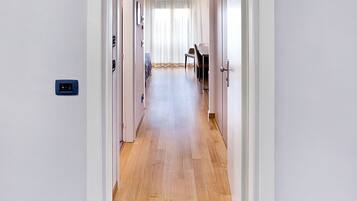 A hallway with a wooden floor, white walls, and a blue carpet at the end.