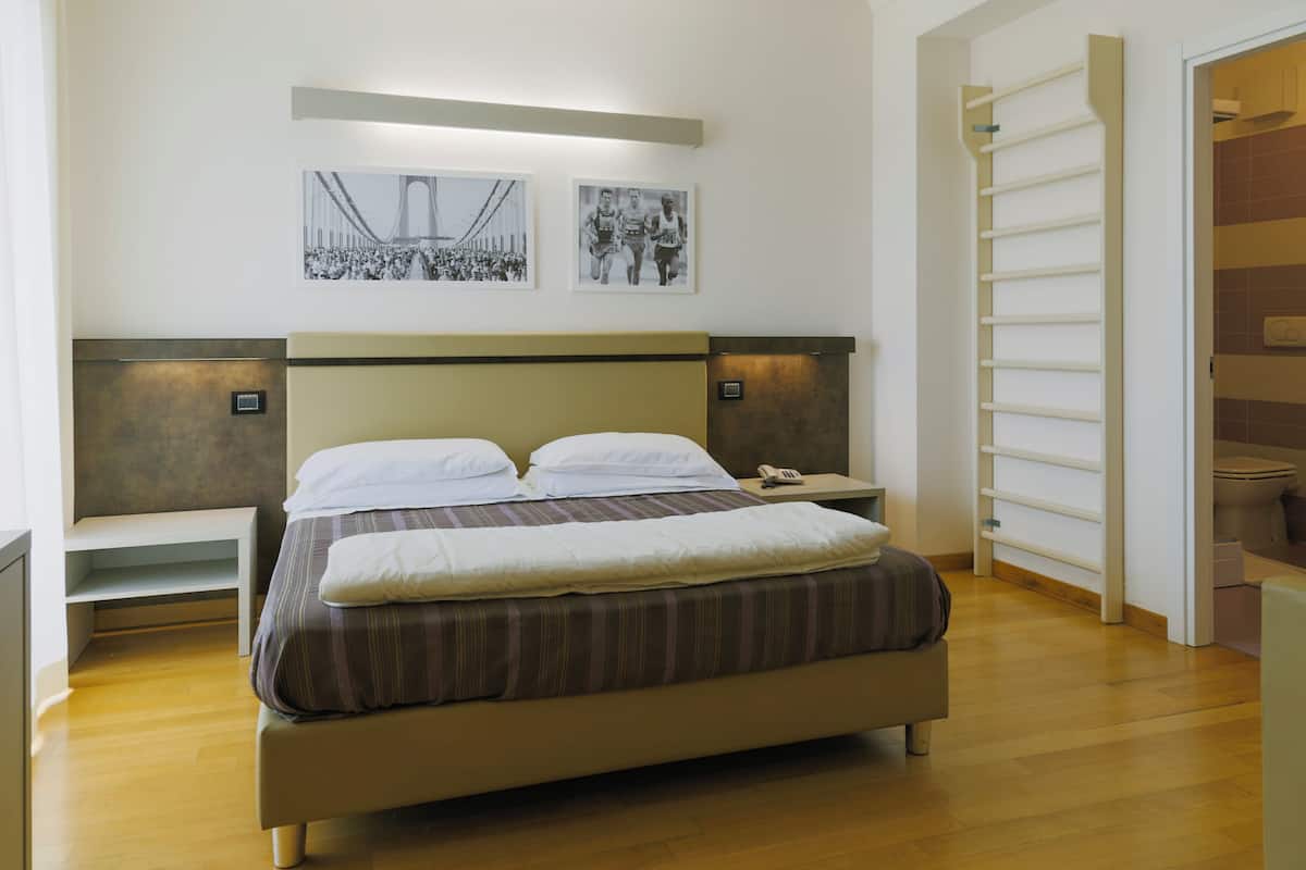 A modern hotel room with a large bed, bedside tables, and a view of the cityscape through the window.
