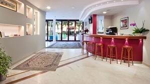 Een moderne hotellobby met een gebogen receptiebalie, barstoelen en een groot vloerkleed.