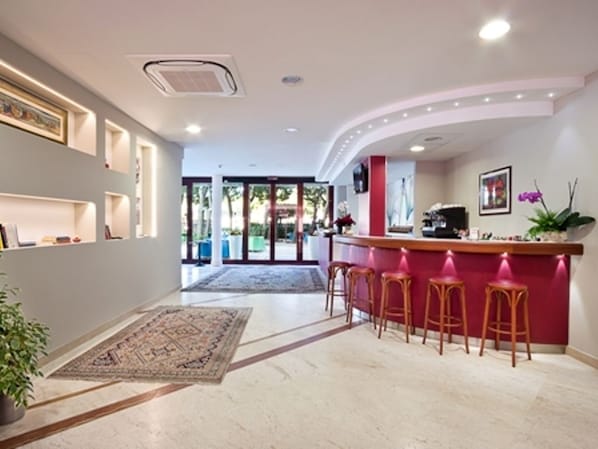 A modern hotel lobby with a curved reception desk, bar stools, and a large rug. - Hotel Sporting (San Benedetto del Tronto)
