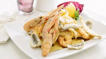 Une assiette de fruits de mer frits, comprenant des crevettes et des calamars, servie dans une assiette blanche et agrémentée d’une tranche de citron et d’une fleur.