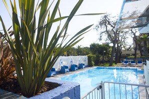 Una piscina con sillas azules, una planta grande y un edificio al fondo.