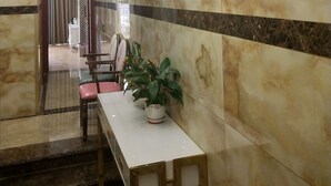 A hotel lobby with marble walls, a chandelier, a long reception desk, and a potted plant.