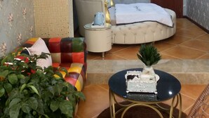 A bedroom with a round bed, a sofa, a small table, and a potted plant.