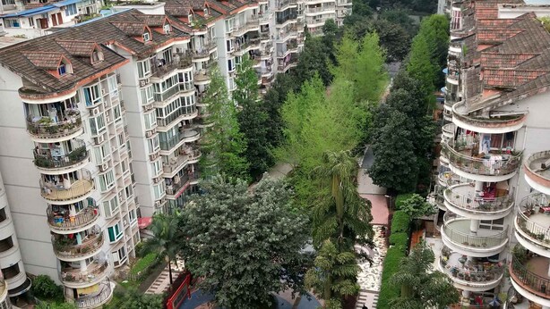 A high-rise residential building with multiple balconies, a central courtyard with trees, and a small bridge over a water feature.