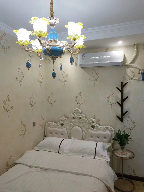 Une chambre avec un lit blanc, un lustre décoratif, un papier peint à motifs floraux et un appareil de climatisation.